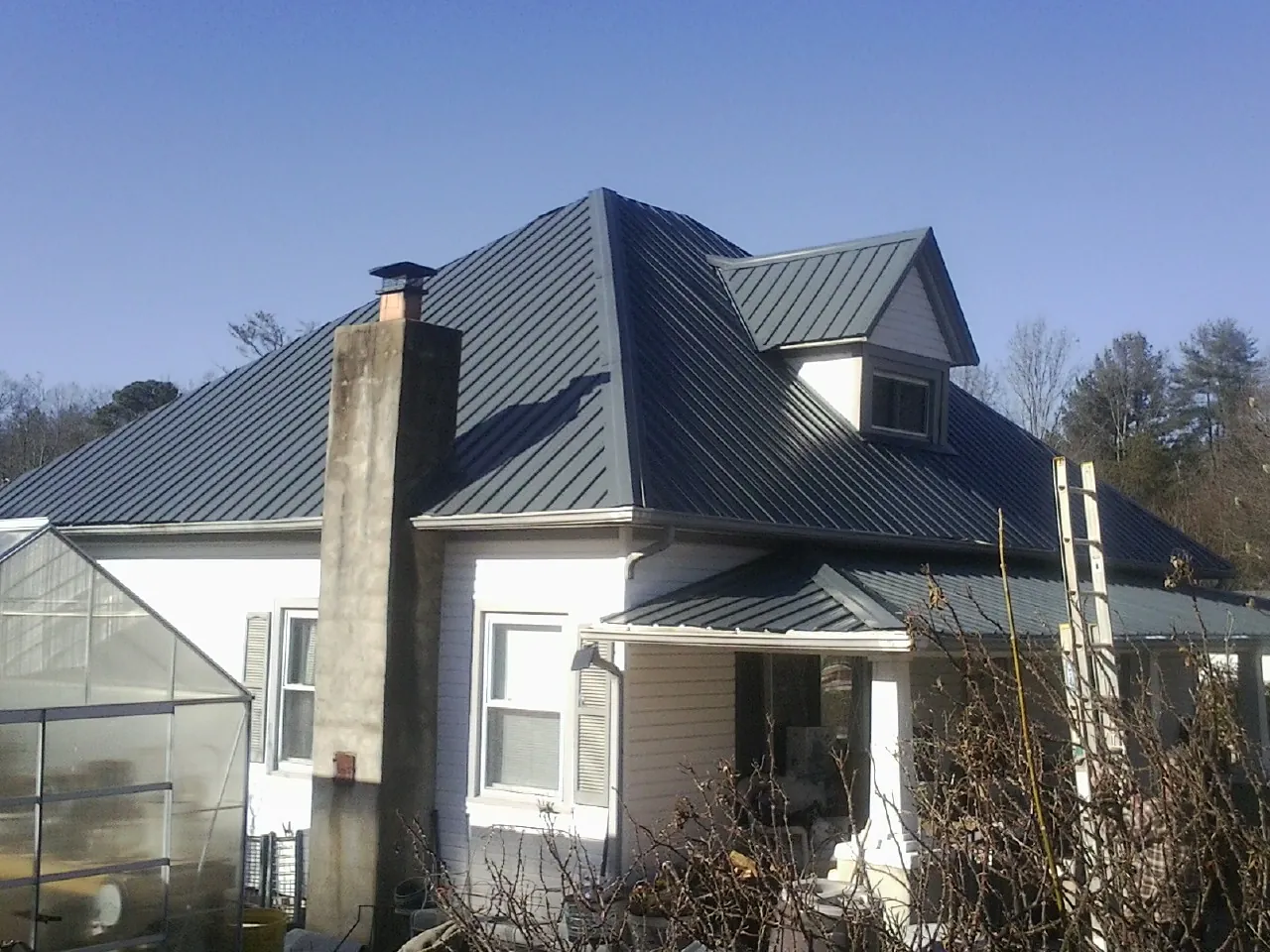 Dark blue standing seam metal roof on a white farmhouse with dormer — Slate & Tile Roof Repair by Roofing Brothers in Montezuma