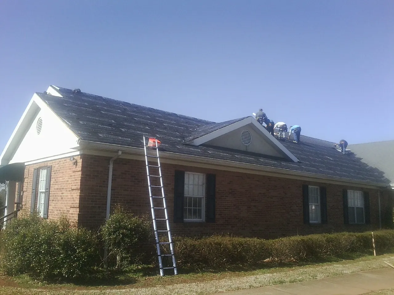 Crew tearing shingles off a brick ranch roof with a ladder set — Emergency Roof Repair work by our crew in Montezuma