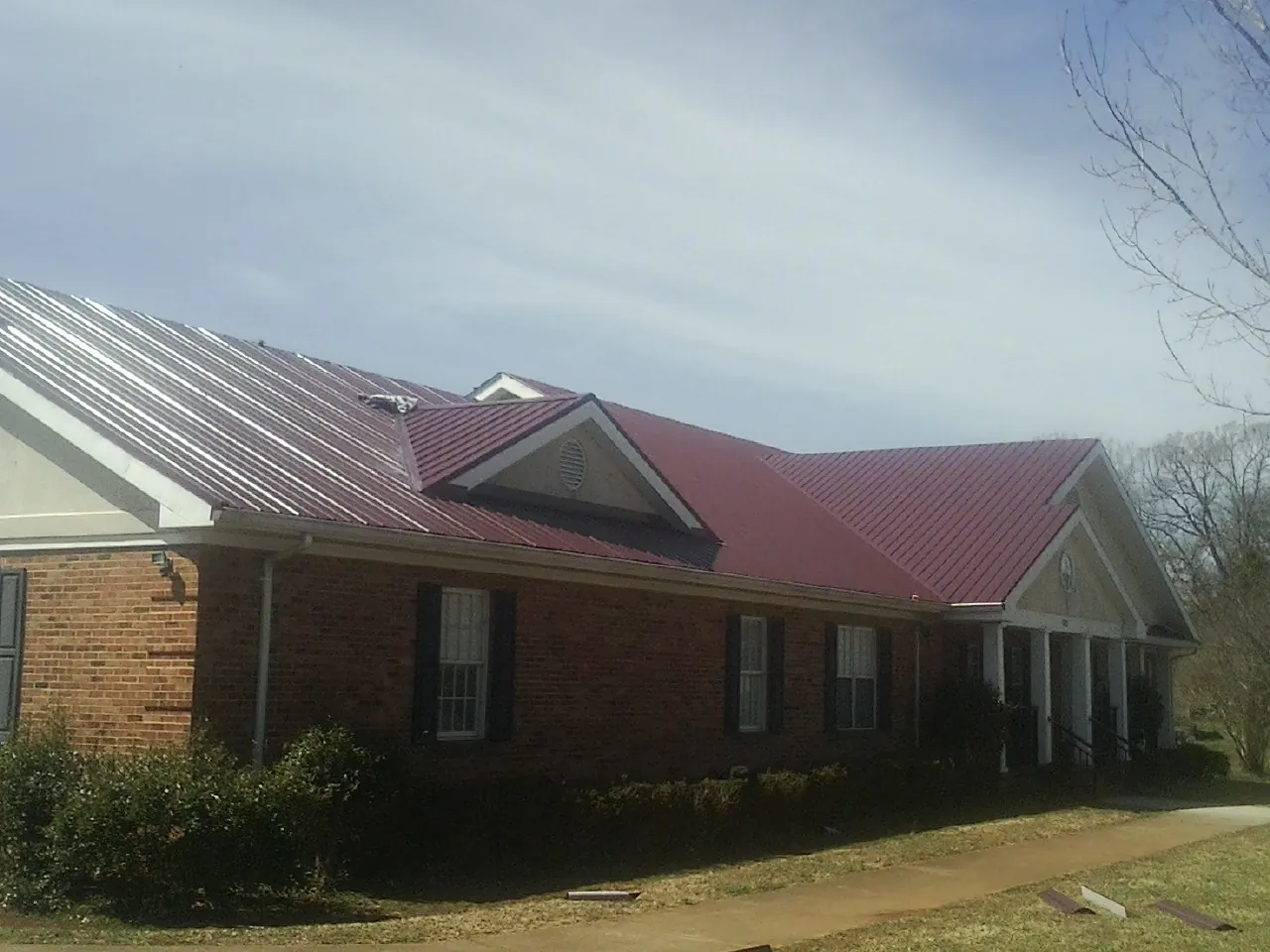 Red metal roof with gabled entries on a long brick building, from a Hail Damage Roof Repair job in Montezuma